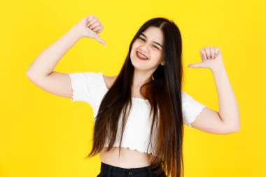 Asyalı, genç, güzel, uzun siyah saçlı kadın modelin portre çekimi. Kırpılmış üst kıyafet giymiş ve sarı arka planda neşeli bir şekilde poz veriyor..