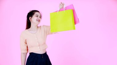 Portre stüdyosu, diş teli takan ve pembe arka planda gülümseyen renkli alışveriş torbaları sunan Asyalı genç ve mutlu alışverişçi kadını çekti..