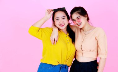 İki Asyalı neşeli arkadaş ya da kız kardeşin, diş telleri ve gözlükleriyle gülümseyen ve pembe arka planda birlikte komik hareketler yaptığı yakın plan çekimleri..