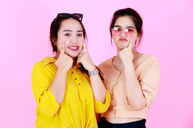 İki Asyalı neşeli arkadaş ya da kız kardeşin, diş telleri ve gözlükleriyle gülümseyen ve pembe arka planda birlikte komik hareketler yaptığı yakın plan çekimleri..