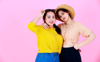 İki Asyalı neşeli arkadaş ya da kız kardeşin, diş telleri ve gözlükleriyle gülümseyen ve pembe arka planda birlikte komik hareketler yaptığı yakın plan çekimleri..