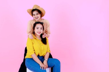 Güneş gözlüklü ve gülümseyen şapkalı, pembe arka planda poz veren iki Asyalı genç, neşeli at kuyruklu kız ya da kız kardeş modelin portre çekimi..