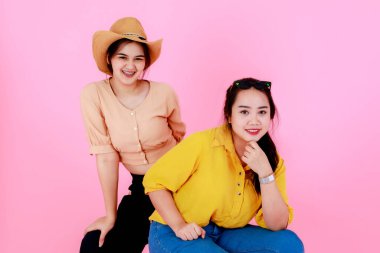 Güneş gözlüklü ve gülümseyen şapkalı, pembe arka planda poz veren iki Asyalı genç, neşeli at kuyruklu kız ya da kız kardeş modelin portre çekimi..