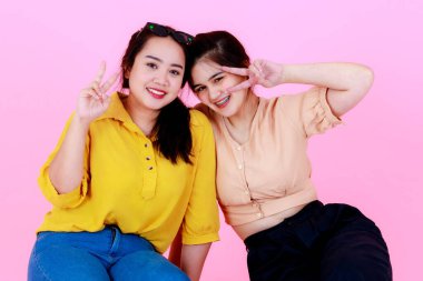 İki Asyalı neşeli arkadaş ya da kız kardeşin, diş telleri ve gözlükleriyle gülümseyen ve pembe arka planda birlikte komik hareketler yaptığı yakın plan çekimleri..