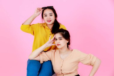 Güneş gözlüklü ve gülümseyen şapkalı, pembe arka planda poz veren iki Asyalı genç, neşeli at kuyruklu kız ya da kız kardeş modelin portre çekimi..
