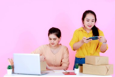 Stüdyo, iki Asyalı mutlu, başarılı, profesyonel kadın girişim küçük iş kadını, gülümseyen ve pembe arka planda birlikte çalışan iş kadını çekti..