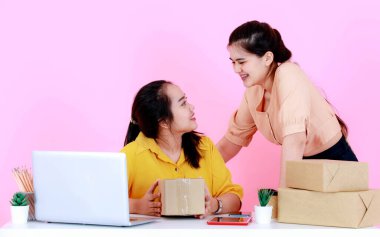 Stüdyo, iki Asyalı mutlu profesyonel kadın girişim küçük iş kadını gülümseyen bir iş kadını, müşteri pembe arka planda ürünler sipariş ettiğinde zafer için yumruklarını kaldırır..