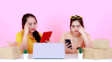 Portre stüdyosu iki mutsuz Asyalı kadını vurdu. Endişeli kadın girişimci iş kadını el ele tutuşurken pembe arka planda müşterilerini kaybetmekte sorun yaşıyor..