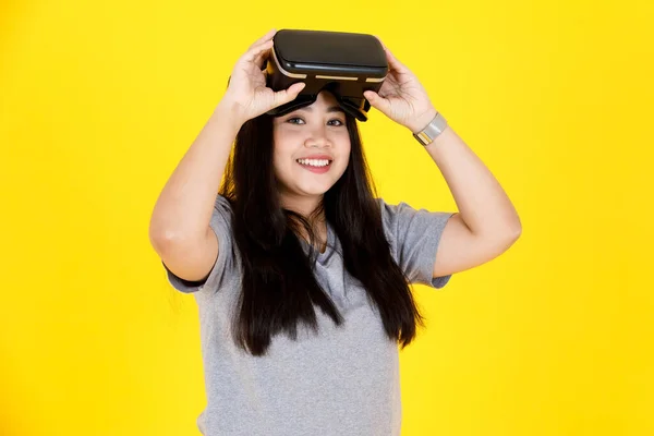 アジアの幸せな若いぽっちゃり長い黒髪の女性ゲーマーモデルのポートレートスタジオショットでカジュアル衣装笑顔身に着けている大きな仮想現実Vrカメラゴーグルコンソールゲーム黄色の背景に — ストック写真