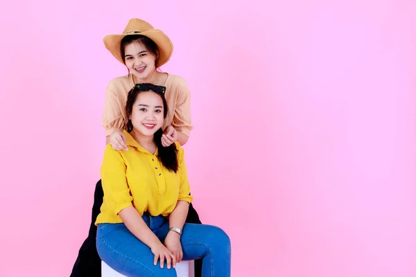 ポートレートスタジオショットの二つのアジアの若い陽気な美しいポニーテール女性の友人や姉妹モデルでカジュアル服でブレースサングラスと帽子の笑顔見ますカメラポージングオンピンクの背景 — ストック写真