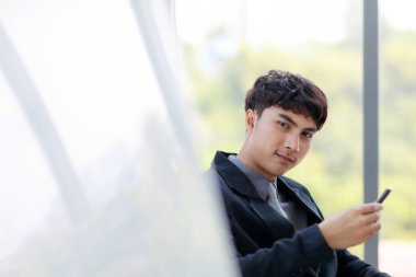 Modern ofiste oturan ve akıllı telefon kullanan yakışıklı Asyalı iş adamının yakın plan fotoğrafı..