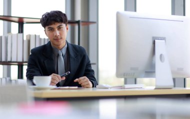 Ön planda, siyah takım elbiseli yakışıklı Asyalı işadamının modern ofiste kanepede oturup kahve içerken görüntüsü bulanık..