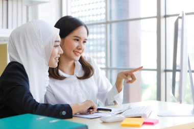 Asyalı iş kadını ve Müslüman patronun yakın plan çekimleri modern ofiste bilgisayarla mutlu bir ruh haliyle dokümanlarını tartışıyor..