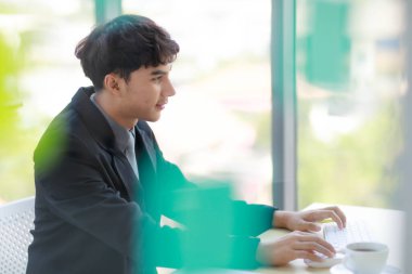 Yakışıklı Asyalı iş adamının modern bir ofiste günlük işleri için bilgisayar kullanmasını yakından çek. Önplanda renkli bulanık.
