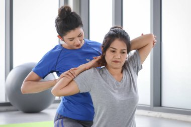 Güzel yoga kadın eğitmeni olgun bir öğrenci için vücut esneme hareketleri öğretirken aynı zamanda spor salonunda spor ayakkabısı pozisyonu almak için paspasların üzerinde oturuyor..