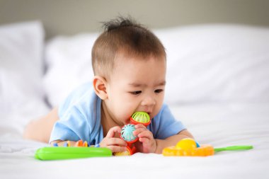 Sevimli ve masum küçük Asyalı bebek renkli çocuklarla oynaşmaktan zevk alıyor. Karnının üstünde yatarken. Tatlı çocuk, çocuk odasında nesneleri tutarak fiziksel şekil ve renk gölgesi öğreniyor..