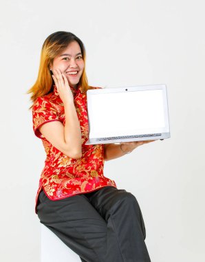 Portre stüdyosu, kırmızı Çin geleneksel Cheongsam Qipao tişörtü giyen Asyalı kadın modelin beyaz arka planda boş ekran dizüstü bilgisayar ürünü sunumunu elinde tutarken çekilmiş..