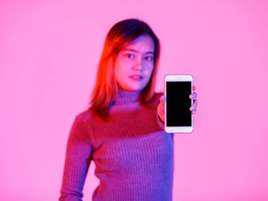 Asyalı genç bayan model, gri kaplumbağa yakalı, kazaklı, pembe ışıklı arka plandaki kameraya bakın..