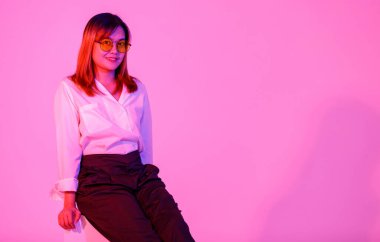 Portre stüdyosu Asyalı kendine güvenen genç bayan girişimci modelini turuncu gözlüklü, gözlüklü pembe ışık arka planında kameraya poz vererek çekti..