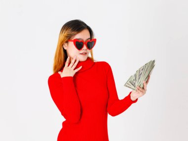 Asyalı özgüvenli kadın moda işkadını modelinin kalp şeklinde gözlüklü, modaya uygun kırmızı elbiseli, beyaz arka planda bir dolar nakit banknot taşıyan bir portre resmi..