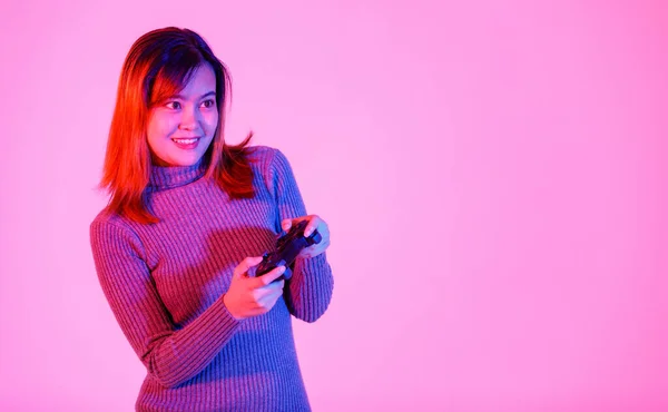 アジアの幸せな若いですティーン女性モデルゲーマーのスタジオショットでグレーTurtleeckドレス立って笑顔開催3DビデオゲームとともにDualshackコンソールジョイスティックで手にピンクの光の背景 — ストック写真