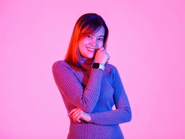 ポートレートスタジオショットアジアの都市トレンディーな女性モデルでグレーTurtleeckセーター立って笑顔見ますカメラクロス腕ショー空白の画面スマートウォッチガジェット上のピンクの光の背景 — ストック写真