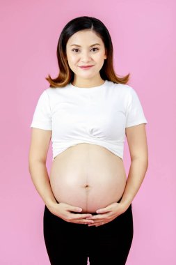 Asyalı, genç, mutlu, hamile bir kadının portre çekimi. Anne kameraya bakıyor. Açık tişört, karnına dokunuyor..