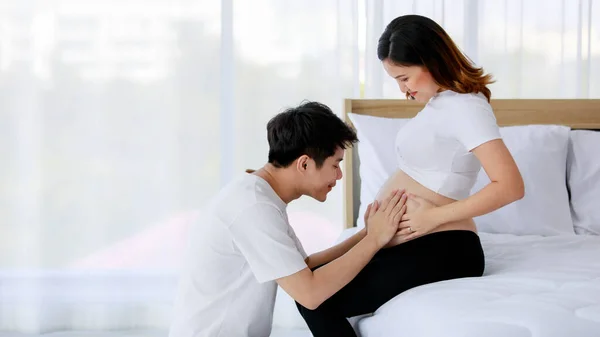 アジアの若いです幸せな愛とサポート夫座っていますと美しいです妊娠中の赤ちゃん妻裸大きな腹おなか胃座っています上のベッドルームで自宅 — ストック写真