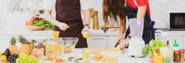 Önlüklü, tanınmayan bir çift modern hafif mutfakta çeşitli ürünler ve mikserlerle birlikte yemek hazırlıyor.