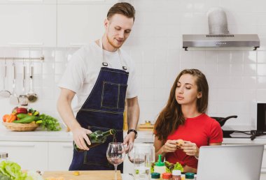 Anonim çiftler bardaklara alkol dökerken modern netbook 'ta hafif modern mutfakta ürünlerle sörf yapıyorlar.