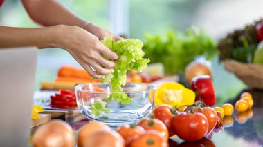 Sağlıklı vejetaryen yemekleri pişirmek için doğal malzemeyi hazırlamak için şefin elleriyle cam kaseye koyduğu taze organik sebzeler. Mutfak masasında olgun meyve, domates, soğan ve dolmalık biber menüsü..