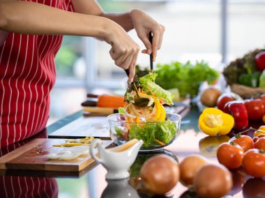 Sağlıklı vejetaryen yemekleri pişirmek için doğal malzemeyi hazırlamak için şefin elleriyle cam kaseye koyduğu taze organik sebzeler. Mutfak masasında olgun meyve, domates, soğan ve dolmalık biber menüsü..