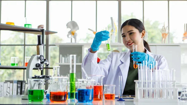 アジアの女性科学者や生物学研究者は ガラス管内の化学的液体反応を観察し 調査機器や顕微鏡の科学研究室での化学実験のビーカーを楽しむ — ストック写真