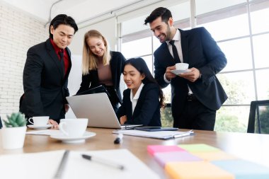 Bir grup pozitif çok ırklı iş arkadaşı modern konferans odasındaki masada netbook incelerken kameraya bakıyor.
