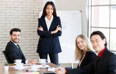 Bir grup çok ırklı iş adamı resmi giysiler içinde yönetim kurulundaki masada tablolar ile kameraya bakarken kameraya bakıyorlar.