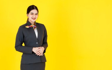 Asyalı profesyonel, başarılı, kendine güvenen, resmi üniformalı, eşarplı, sarı arka planda poz veren ve gülümseyen kadın hostesin portre çekimi..