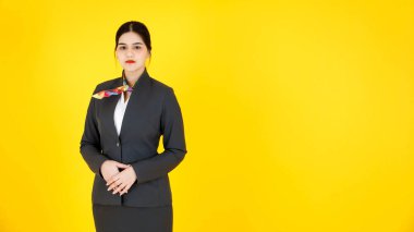 Asyalı profesyonel, başarılı, kendine güvenen, resmi üniformalı, eşarplı, sarı arka planda poz veren ve gülümseyen kadın hostesin portre çekimi..