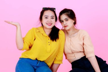 İki Asyalı neşeli arkadaş ya da kız kardeşin, diş telleri ve gözlükleriyle gülümseyen ve pembe arka planda birlikte komik hareketler yaptığı yakın plan çekimleri..