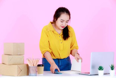 Asya 'nın stüdyo çekimi mutsuz genç bayan girişimci iş kadınını üzdü. Kol saatine bakıyor. Pembe arka planda müşteriler için fazla mesai paketlemesi yapıyor..