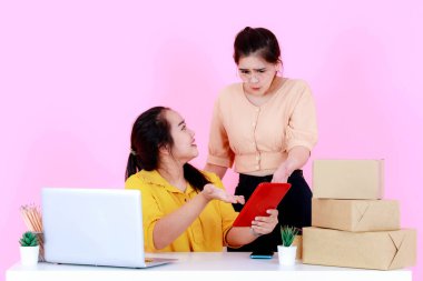 Stüdyo, iki Asya 'lı mutsuz kadın sinirli girişimci iş kadını vurdu. Müşteri stratejisi ve pazarlama verileri hakkında tartıştılar. Pembe arka planda tablette..