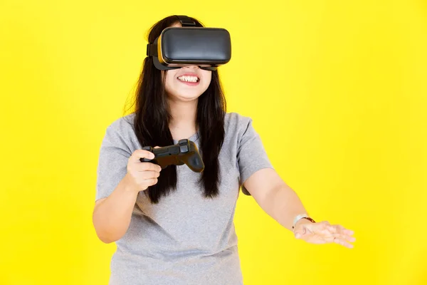亚洲快乐的胖胖的年轻胖胖的黑头发女游戏模特笑着穿着大大的虚拟现实Vr相机护目镜拿着控制杆在黄底玩3D游戏的工作室照片 — 图库照片