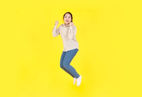 ポートレートスタジオショットのアジアの若い幸せな女性ぽっちゃりぽっちゃりモデルでカジュアル服長袖シャツとデニムジーンズパンツ笑顔見てでカメラジャンプ高運動だけで黄色の背景 — ストック写真
