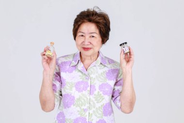 Yaşlı teyze, yaşlı Asyalı kadın, beyaz arka plan konseptinde virüs tedavisi için antibiyotik ilaç olarak hastaneden alınan hapları elinde tutuyor.