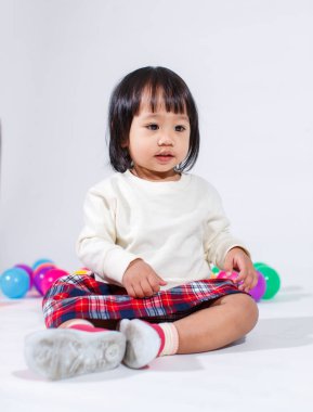 Küçük, şirin, kısa, siyah saçlı, Asyalı, ekoseli etekli, gülen, beyaz arka planda tek başına renkli yuvarlak toplarla oynayan küçük kız modelin stüdyo fotoğrafı..
