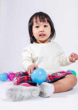 Küçük, şirin, kısa, siyah saçlı, Asyalı, ekoseli etekli, gülen, beyaz arka planda tek başına renkli yuvarlak toplarla oynayan küçük kız modelin stüdyo fotoğrafı..
