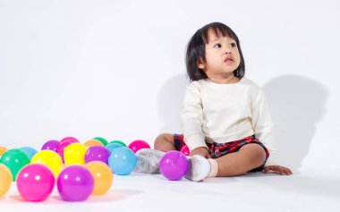 Küçük, şirin, kısa, siyah saçlı, Asyalı, ekoseli etekli, gülen, beyaz arka planda tek başına renkli yuvarlak toplarla oynayan küçük kız modelin stüdyo fotoğrafı..