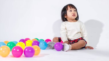 Küçük, şirin, kısa, siyah saçlı, Asyalı, ekoseli etekli, gülen, beyaz arka planda tek başına renkli yuvarlak toplarla oynayan küçük kız modelin stüdyo fotoğrafı..