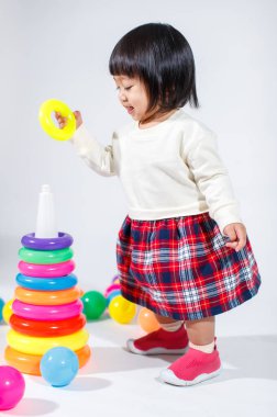 Renkli plastik yüzüklerle oynayan, küçük Asyalı kız bebek modelinin stüdyo fotoğrafı. Renkli plastik halkalar, piramit oyuncakları ve beyaz arka planda küçük toplar.