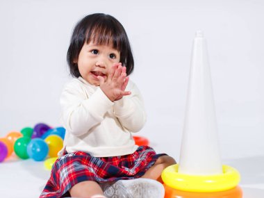 Küçük şirin Asyalı kız bebek modelin stüdyo fotoğrafı. Günlük kıyafetleriyle yerde oturmuş renkli plastik yüzüklerle oynuyorlar. İnşaat piramidi oyuncakları ve beyaz arka planda küçük toplar..