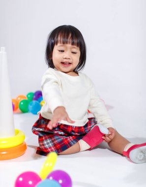 Küçük şirin Asyalı kız bebek modelin stüdyo fotoğrafı. Günlük kıyafetleriyle yerde oturmuş renkli plastik yüzüklerle oynuyorlar. İnşaat piramidi oyuncakları ve beyaz arka planda küçük toplar..